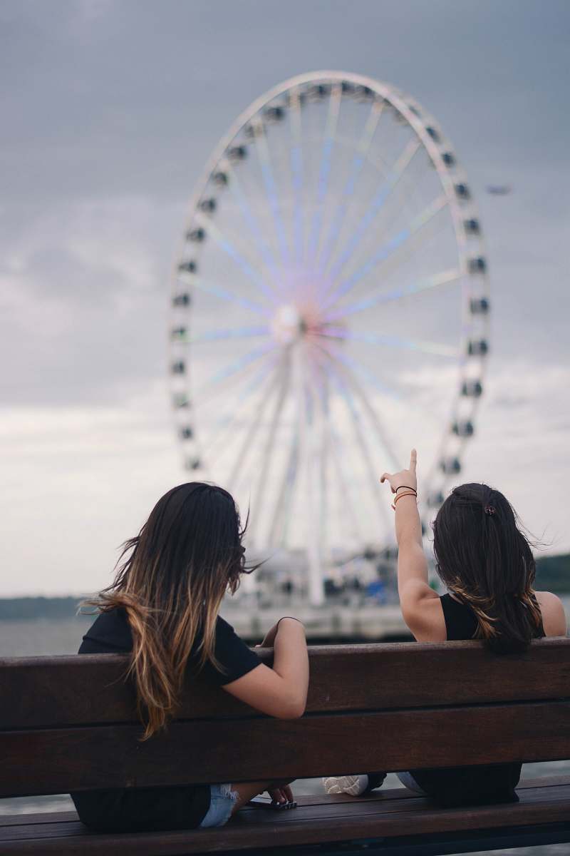 ferris wheel two women sitting on bench pointing white and blue Ferris wheel amusement park